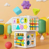 A white Montessori shape sorting cube with colorful plastic shapes and elastic bands is displayed against a light background.
