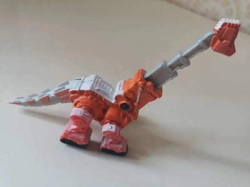 A die-cast dinosaur truck toy with a removable dino figure in orange and gray.