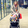 A woman pushing a stroller with a baby wearing sensory toys and a colorful scarf in an outdoor setting.
