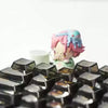A close-up of a collectible keycap blind box featuring an anime-style character with pink hair and blue accents.