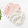 A light pink knitted cotton cardigan sweater laid flat on a white surface.