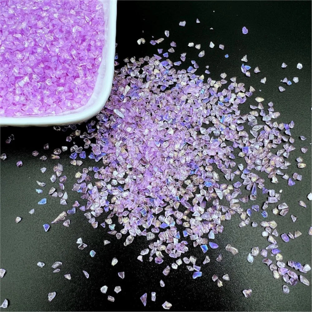 Purple crushed glass crystals scattered on a dark surface next to a white dish.