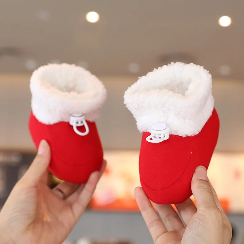 A pair of red baby first walker shoes with fluffy white trim being held by a person.