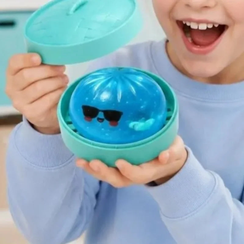 A child holds a teal squishy fidget toy shaped like a glitter shark dumpling with sunglasses inside its box.