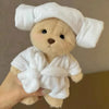A fluffy teddy bear plush wearing a white, textured dress and a matching white head wrap.