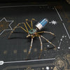 A steampunk metal spider model with long legs and a glass body is displayed on a dark surface.