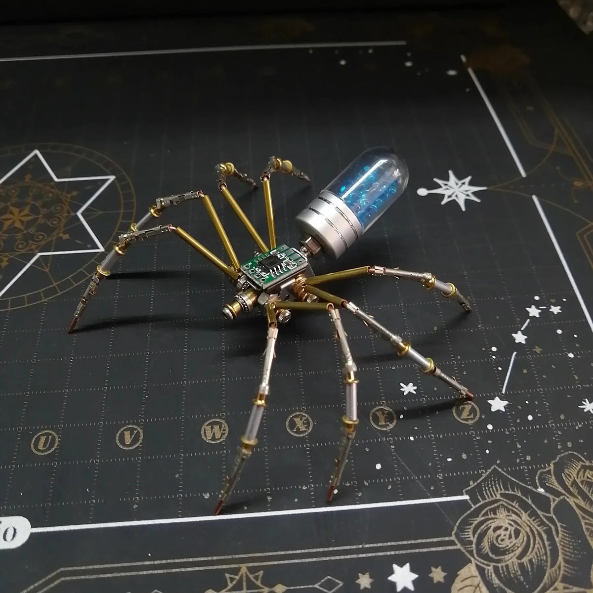 A steampunk metal spider model with long legs and a glass body is displayed on a dark surface.