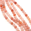 Strands of natural stone round beads in shades of pink, orange, and red for jewelry making