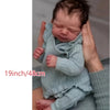 A newborn baby doll with a soft cloth body is being held by hands, shown in a close-up.