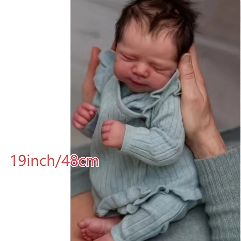 A newborn baby doll with a soft cloth body is being held by hands, shown in a close-up.