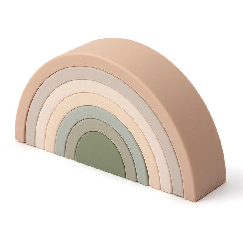 A set of soft silicone rainbow building blocks in pastel shades of pink, beige, and green.