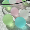 A collection of pastel colored squishy stress cubes, including green, pink, and light blue, resting on a white textured surfa