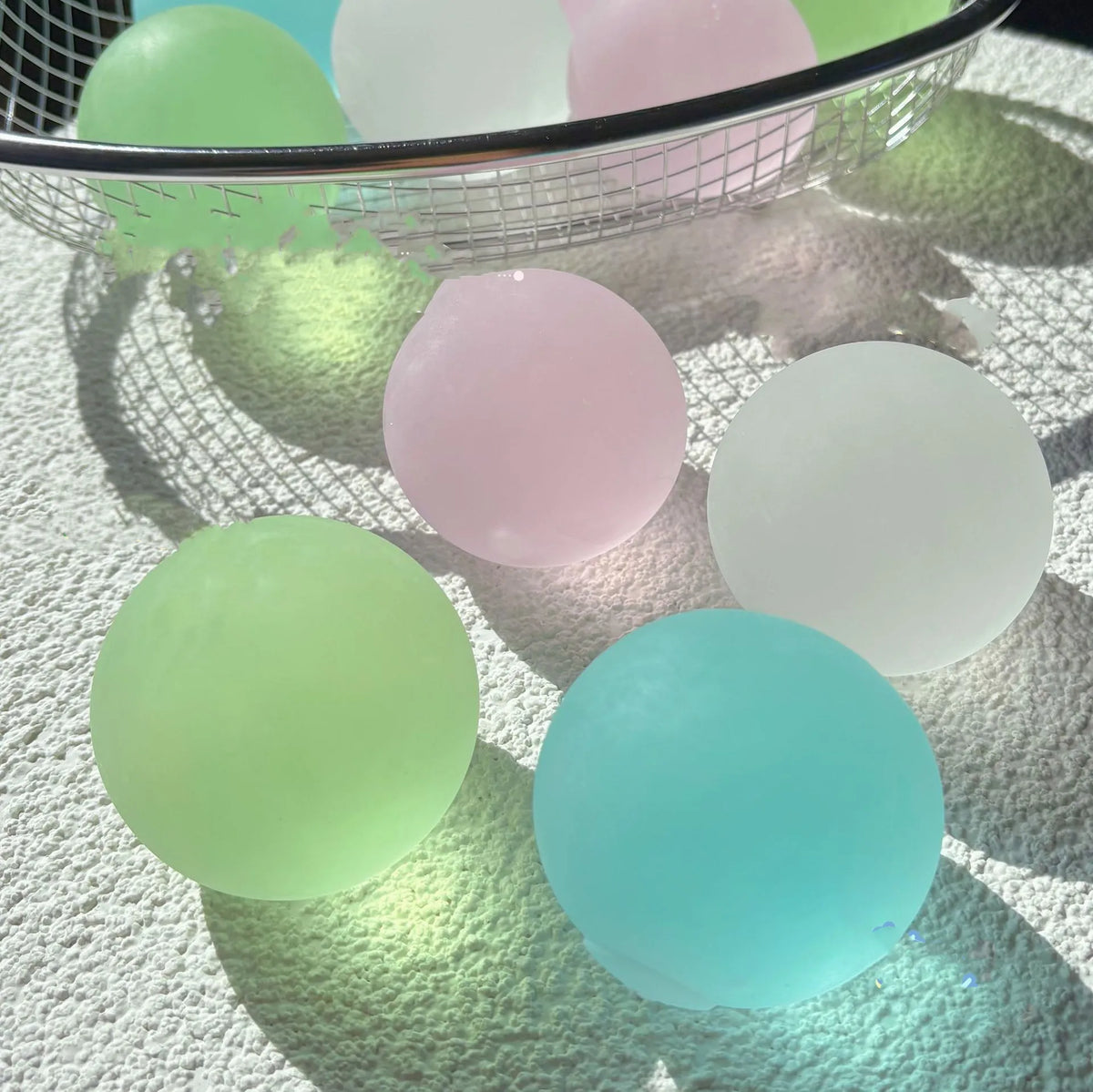 A collection of pastel colored squishy stress cubes, including green, pink, and light blue, resting on a white textured surfa