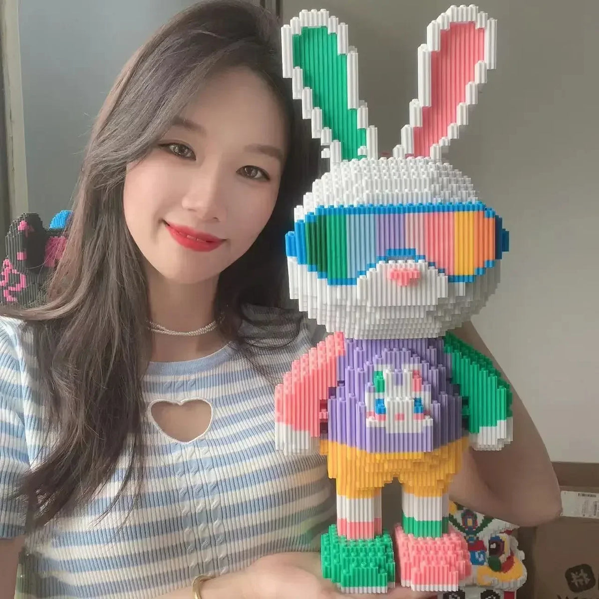 A young woman holds a colorful building block toy shaped like a rabbit and bear, made of micro bricks.