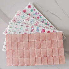 A set of pearl pink acrylic American Mahjong tiles stacked diagonally on a marble surface.