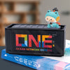 A small blue figurine sits on a black industrial iron storage box labeled Ocean Network Express next to a book.
