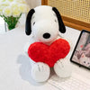A white plush toy of a dog with black ears and a red heart attached, sitting on a white surface.