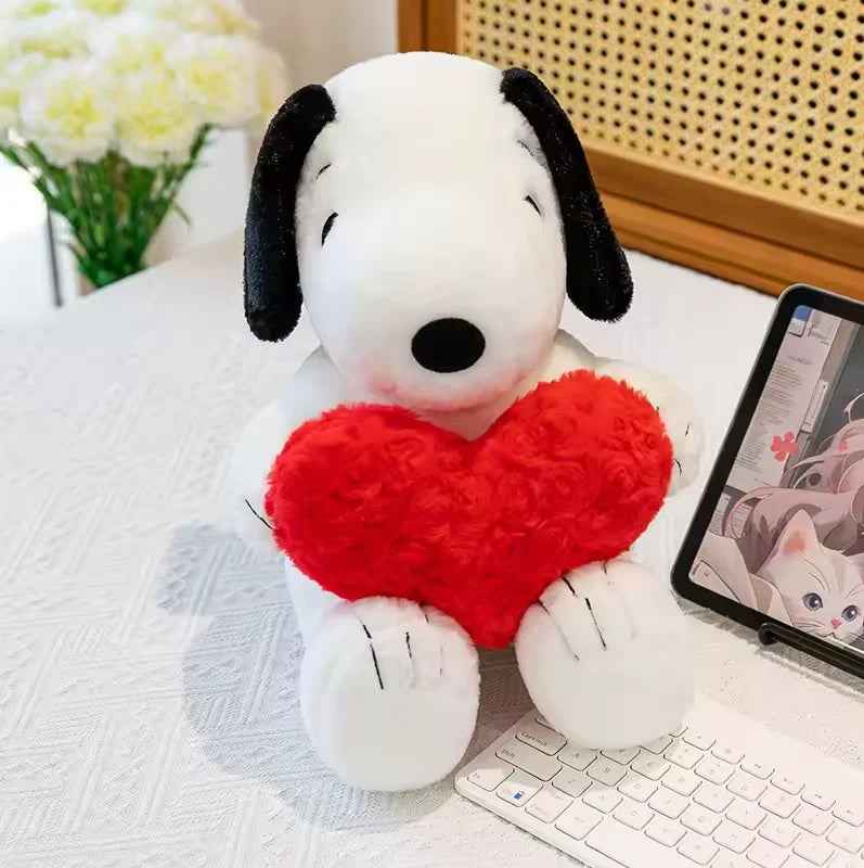 A white plush toy of a dog with black ears and a red heart attached, sitting on a white surface.