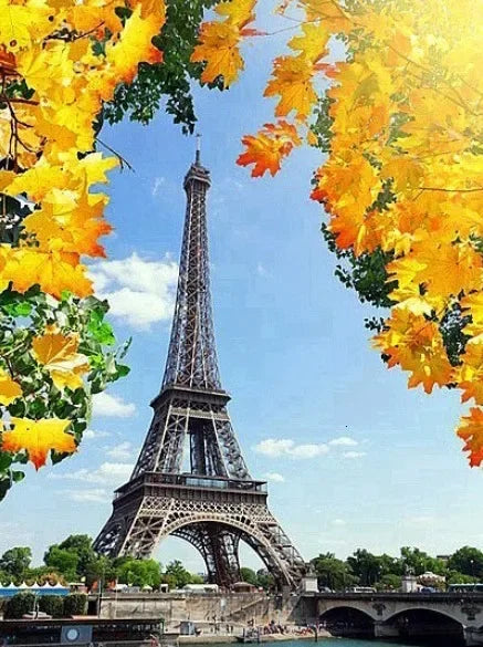 A vibrant view of the Eiffel Tower framed by bright yellow autumn leaves against a blue sky.