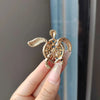 A close-up of a gold rhinestone turtle brooch pin being held by a hand against a light blue background.