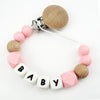 A bracelet made of wooden and pink silicone beads with a clip, featuring the name BABY.