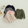 A collection of four knit pullover sweaters in shades of gray, pink, and olive green laid out on a light surface.