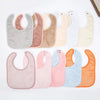 A collection of soft cotton baby bibs in various pastel and neutral colors arranged horizontally.