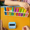 A hand is holding a set of 20 colored bottles arranged in a puzzle format on a yellow surface.