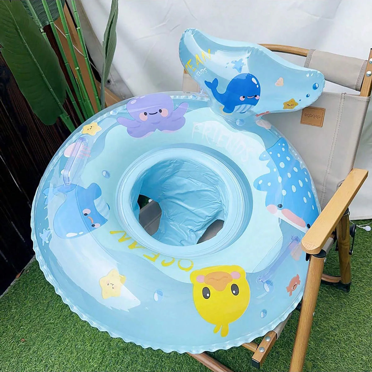 A light blue inflatable baby swim ring with sea animals and a comfortable seat is shown on a green surface.