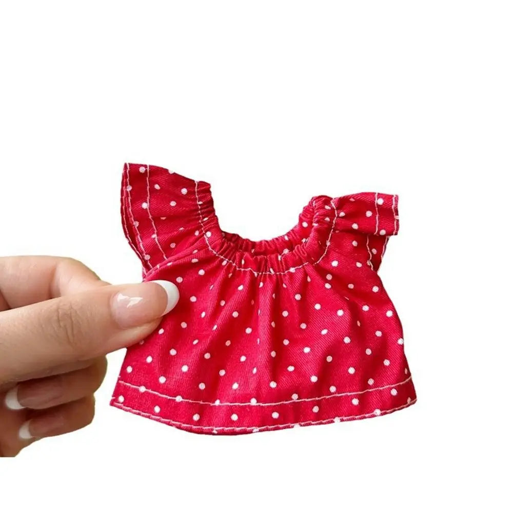 A hand holds a red polka dot top designed for fashion dolls.