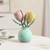 A small vase holds two artificial flowers, one pink and one yellow, on a white table.