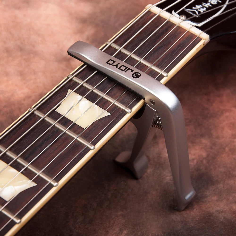A close-up of a silver zinc alloy guitar capo clamped onto the fretboard of a stringed instrument.