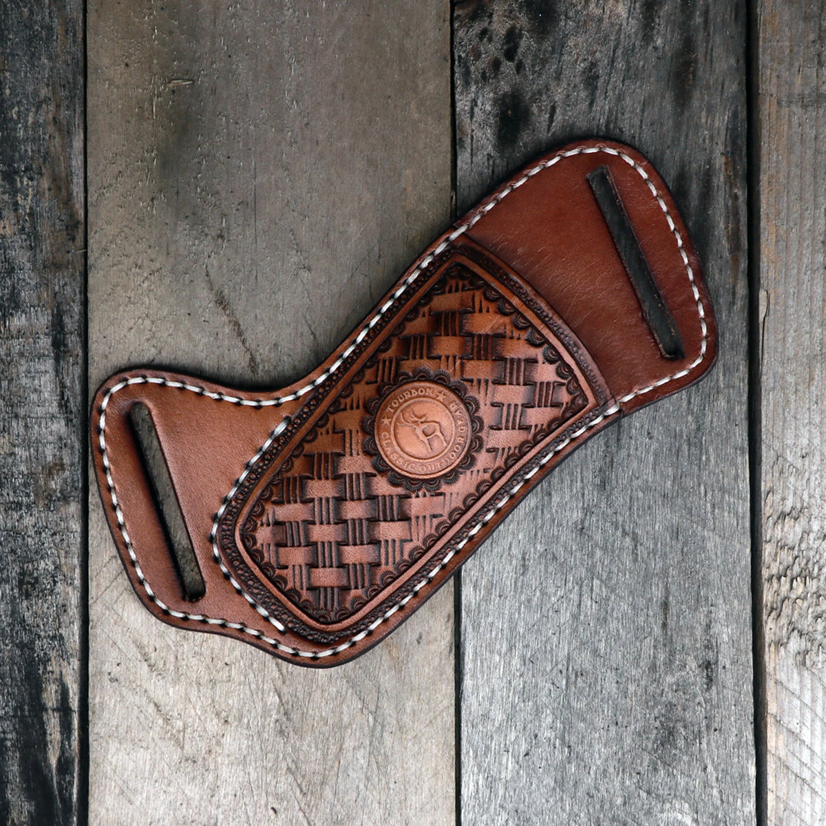 A brown leather knife sheath with a belt loop featuring a woven pattern rests on weathered wooden planks.