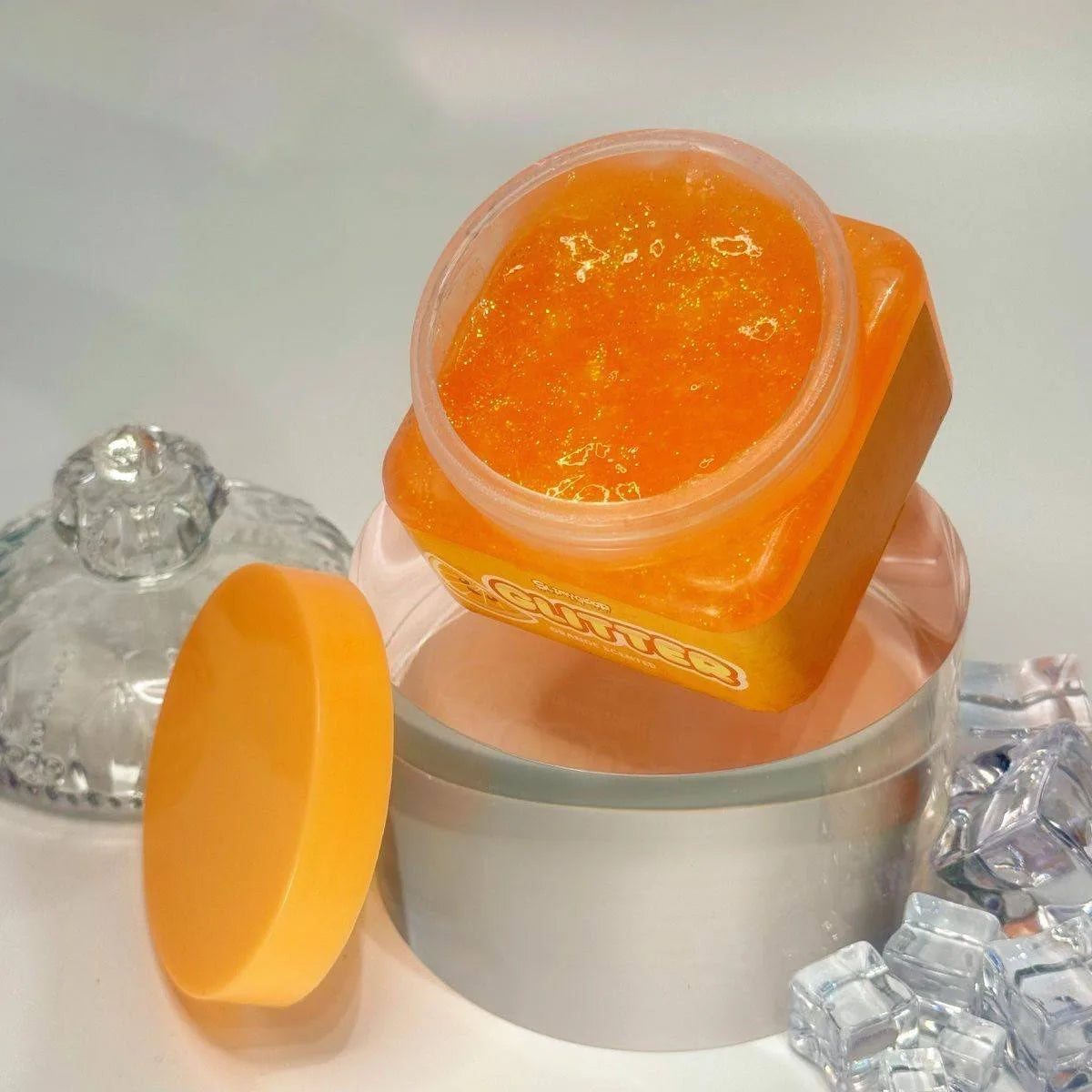 A jar of orange slime is shown next to a yellow blob of slime and clear crystals.