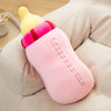 A pink milk bottle plush pillow with a yellow cap and red trim resting on a light-colored fabric.