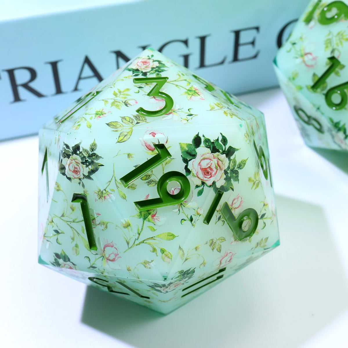A translucent green resin D20 die with floral designs and numbers 1, 3, 6, and 10.