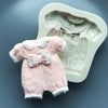A pink silicone cake mold shaped like a baby's outfit with a bow, resting next to a white mold.