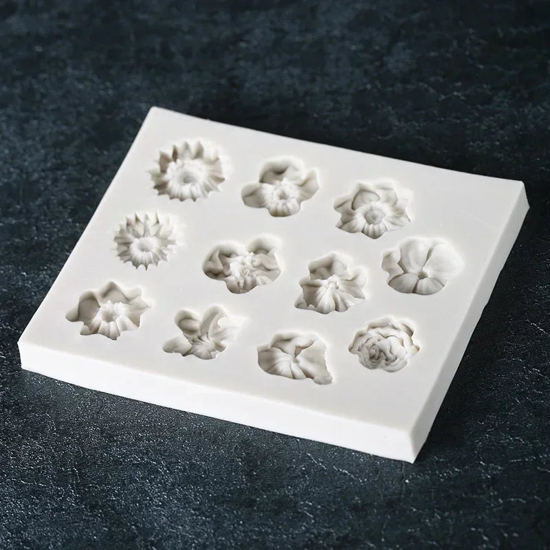 A white silicone mold with various flower shapes, including sunflowers and roses, for chocolate and cake decorating.