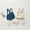 A denim romper for a toddler with pockets and matching light colored shoes displayed on a white background.