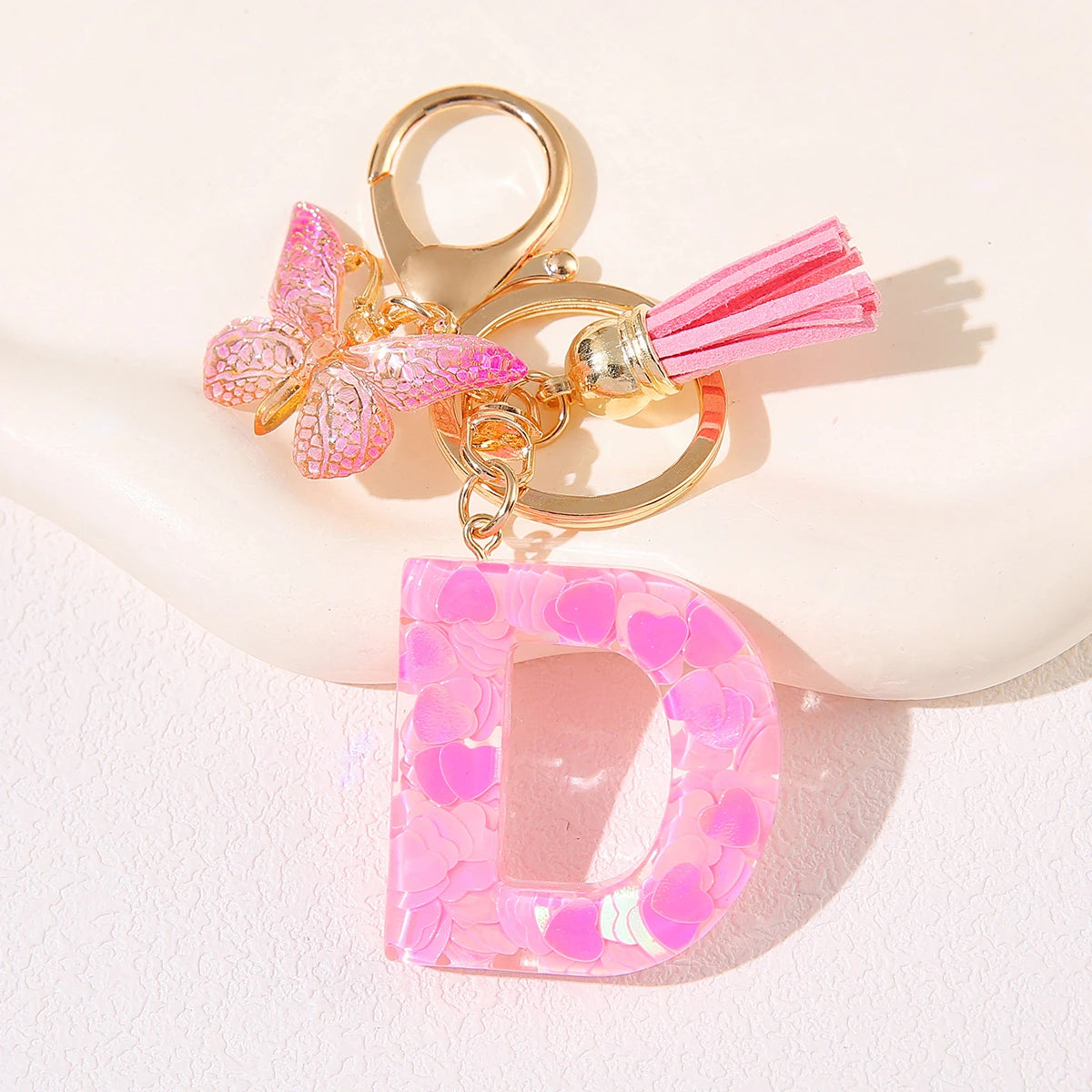 A gold initial heart keychain featuring a pink butterfly charm and a clear pink initial pendant.