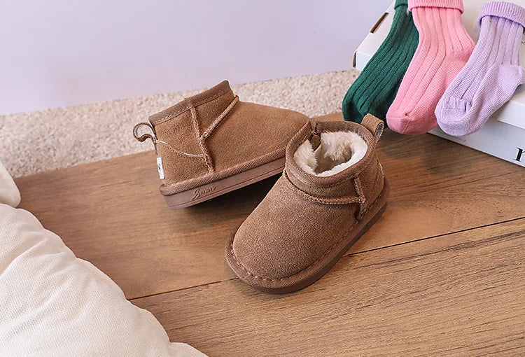 A pair of tan suede winter snow boots and several colorful knitted socks are displayed on a wooden surface.