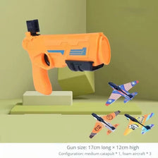 Orange airsoft gun toy and three foam airplanes displayed on a light green surface.
