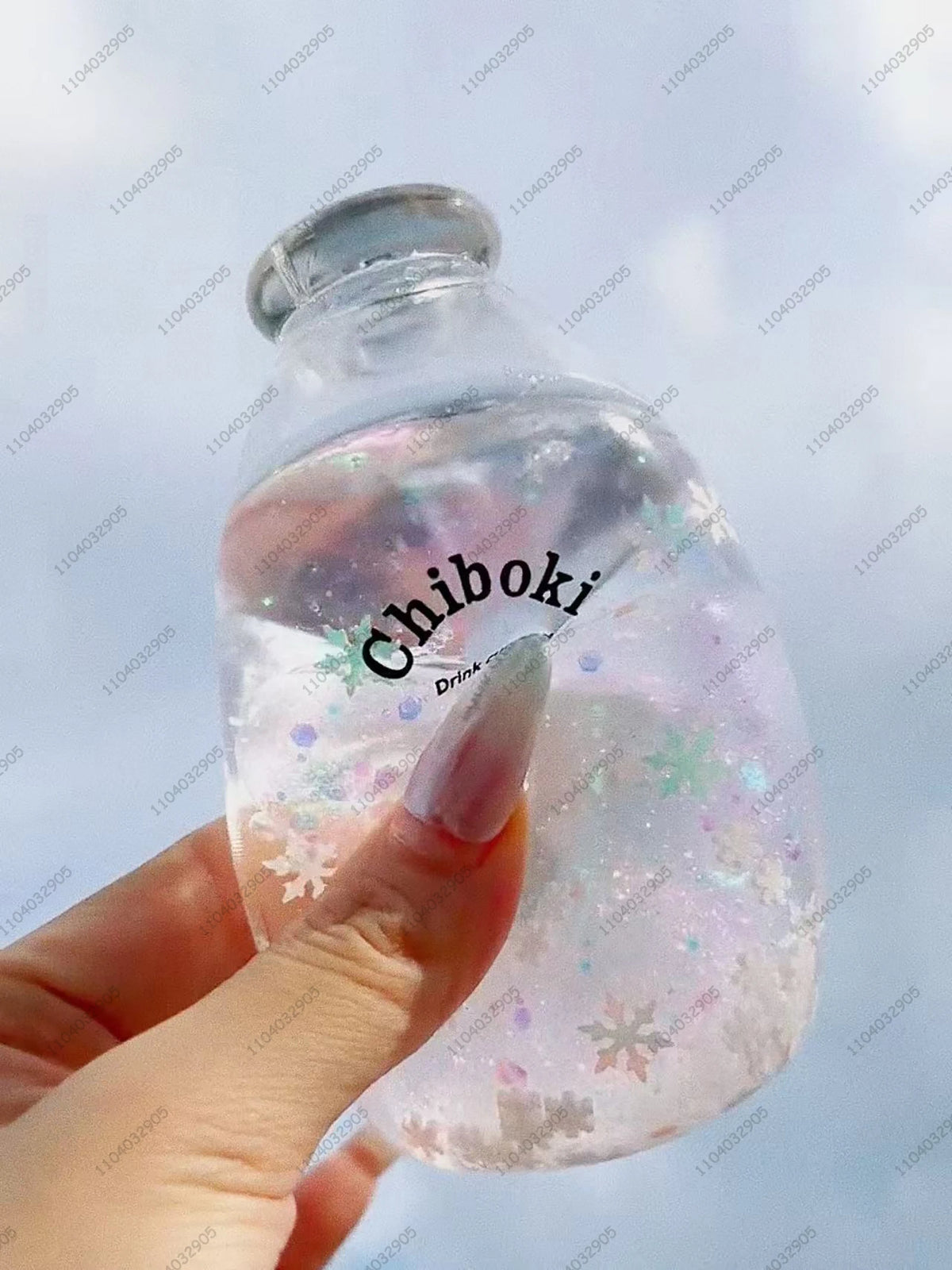 A hand holds a clear bottle filled with liquid and glitter, labeled Chiboki, against a light blue background.
