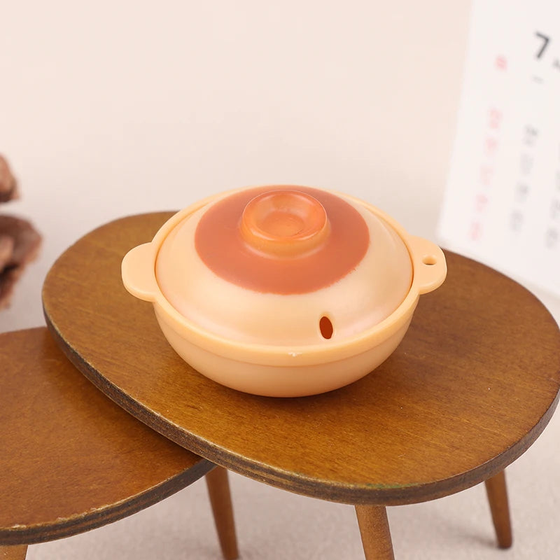 A miniature copper soup pot with a light orange lid resting on a wooden surface.