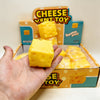 A hand holds a yellow cheese squeeze fidget toy inside its original box.