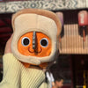 A hand holds an orange Pochita plush doll with large eyes and a gray nose against a blurred background.