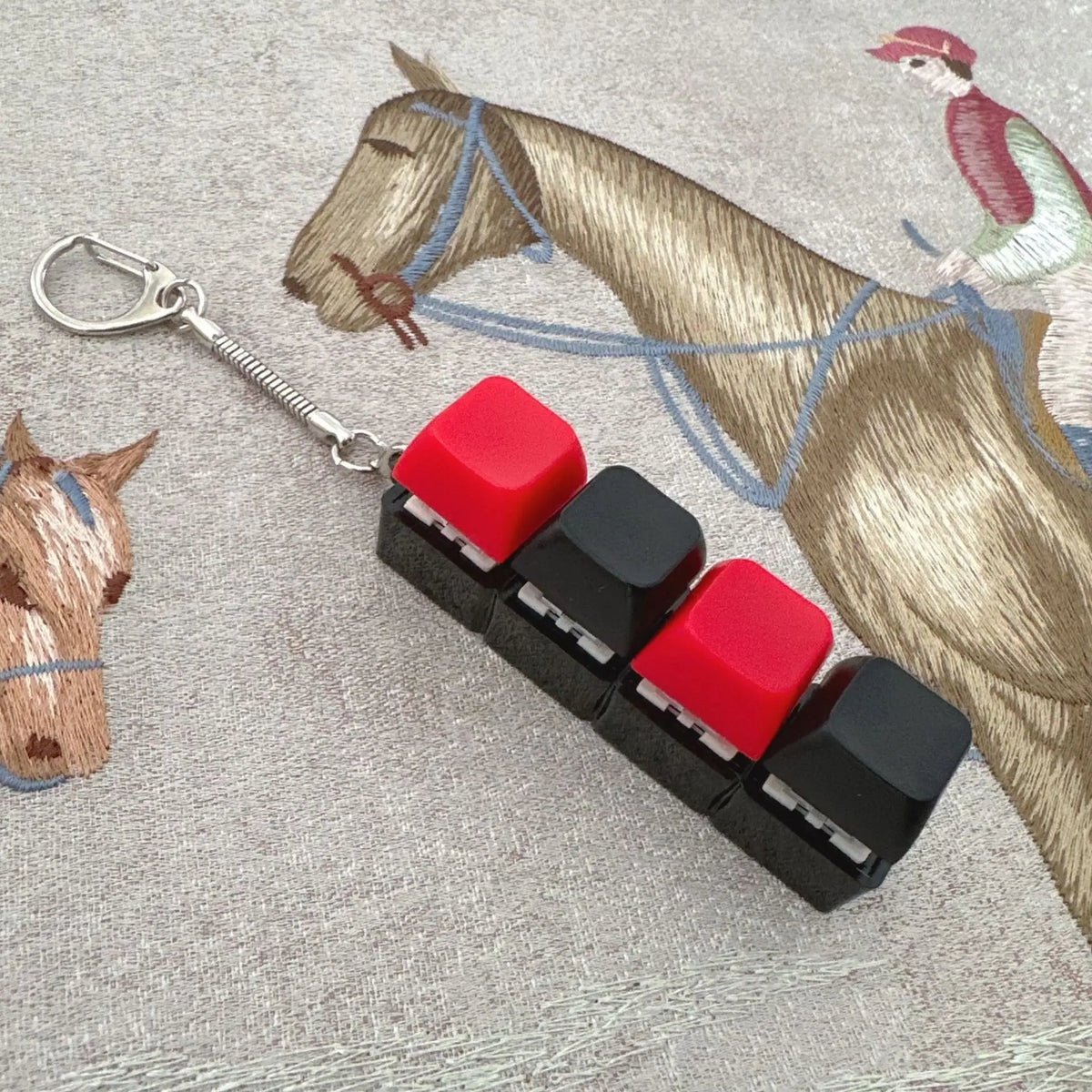 A colorful acrylic keycap fidget keychain with four red and black clicky key buttons is shown next to a horse figurine.