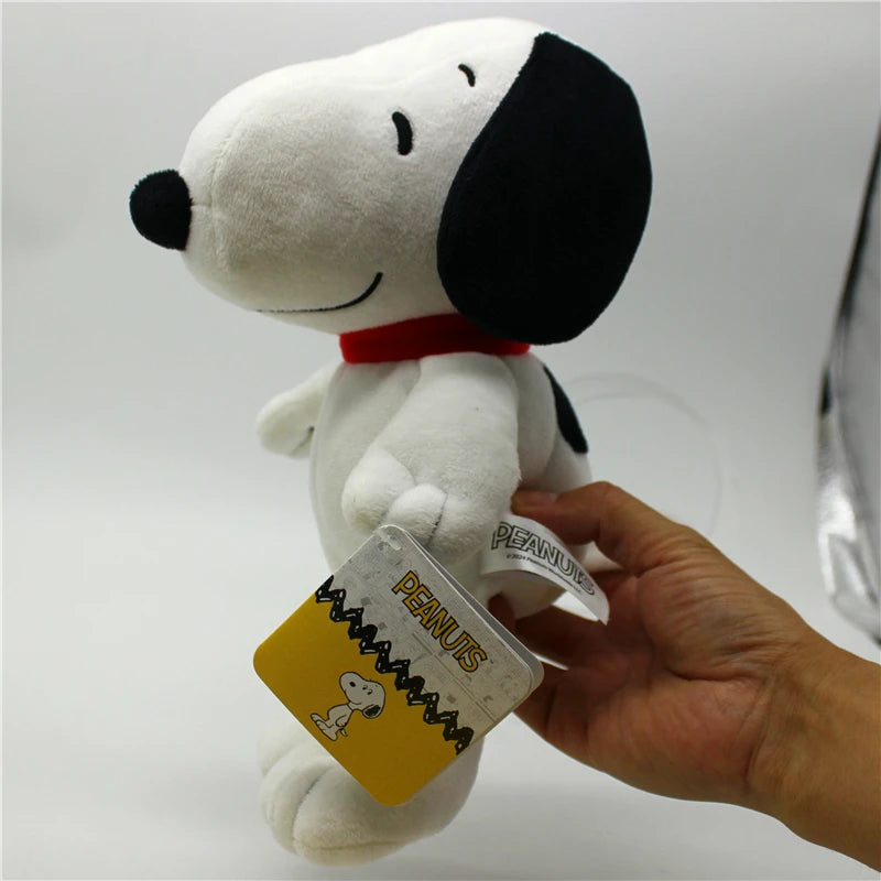 A white Snoopy plush toy with black ears and a red collar is being held by a hand.