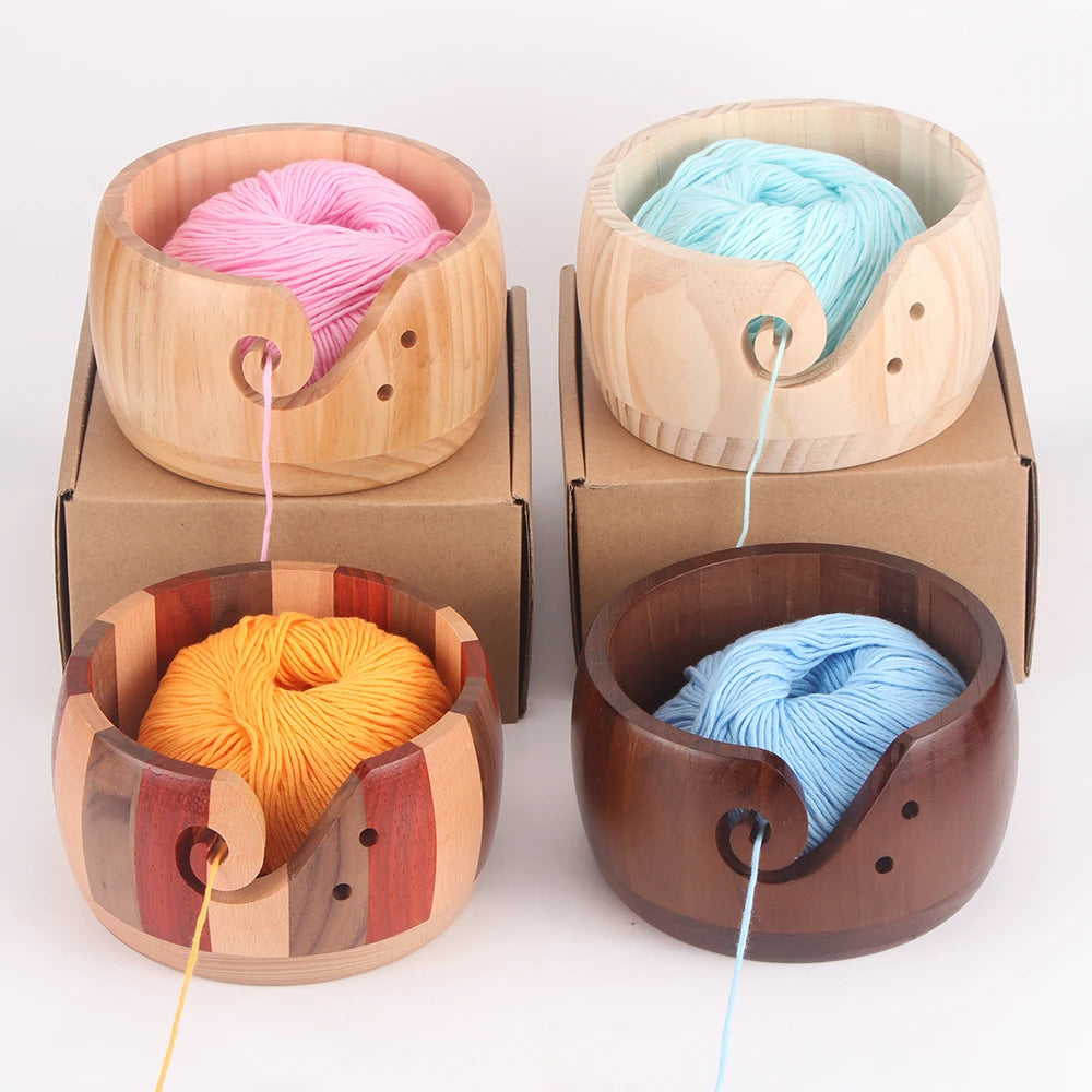 Three handcrafted wooden yarn bowls in pink, light blue, and orange with swirling cutouts.