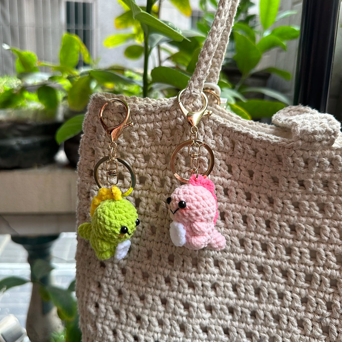 A handmade crochet dinosaur keychain featuring a yellow and green dinosaur charm hanging from a beige crocheted bag.